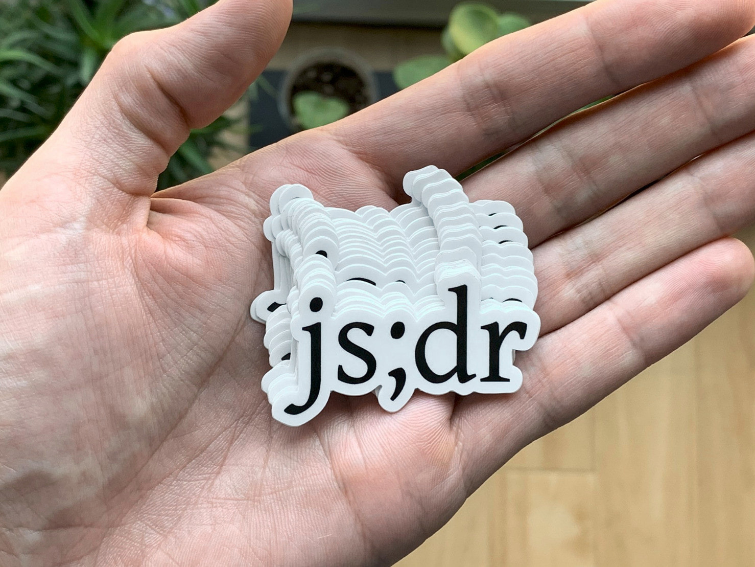 hand holding a pile of outline-cut 'js;dr' stickers, black text on a white background