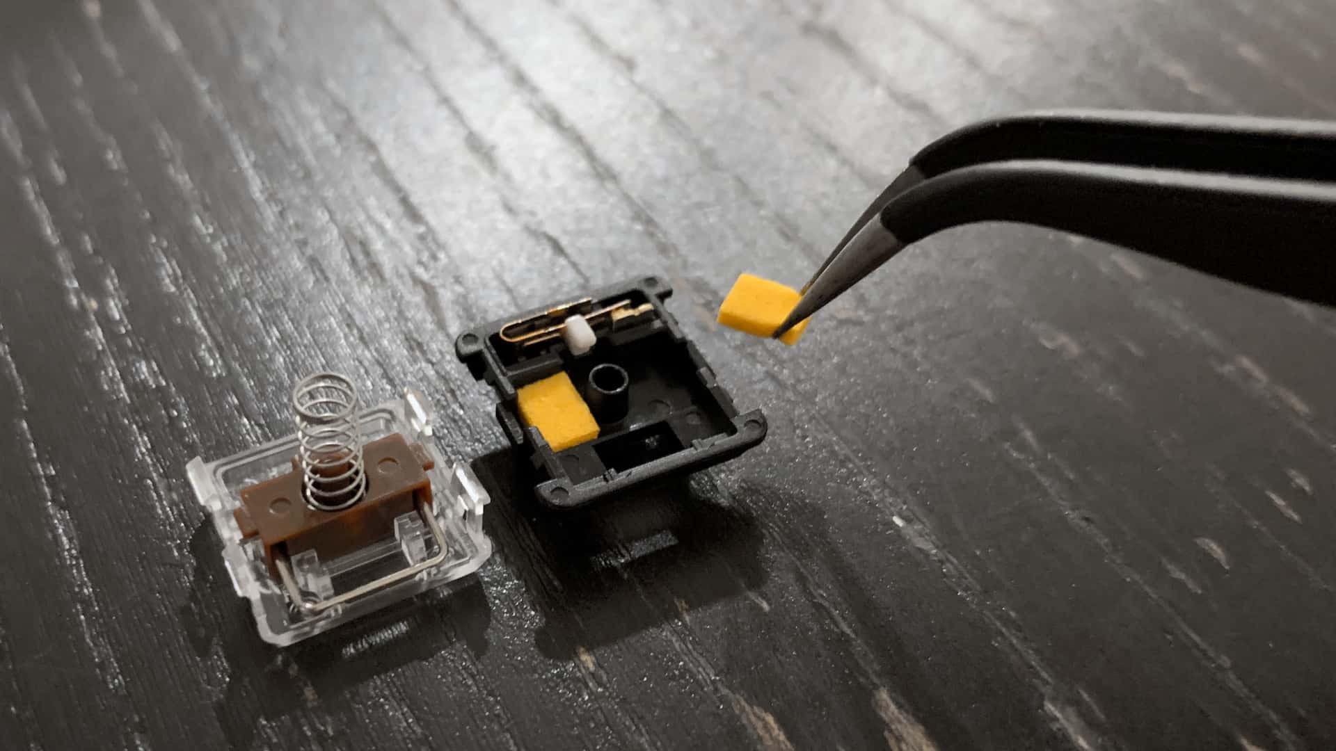 tweezers inserting a yellow foam pad into an opened Kailh “Choc” Brown key switch
