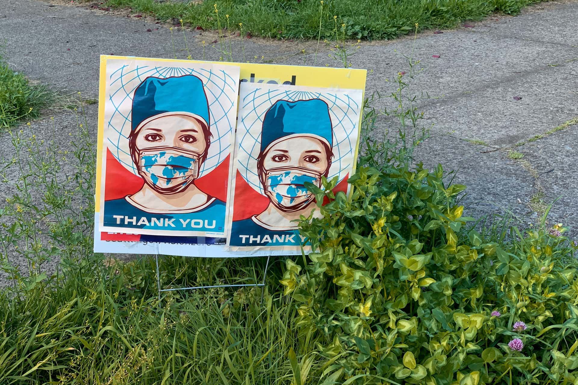 yard sign saying “Thank You” below an illustration of a medical worker wearing a face mask stylized as the earth