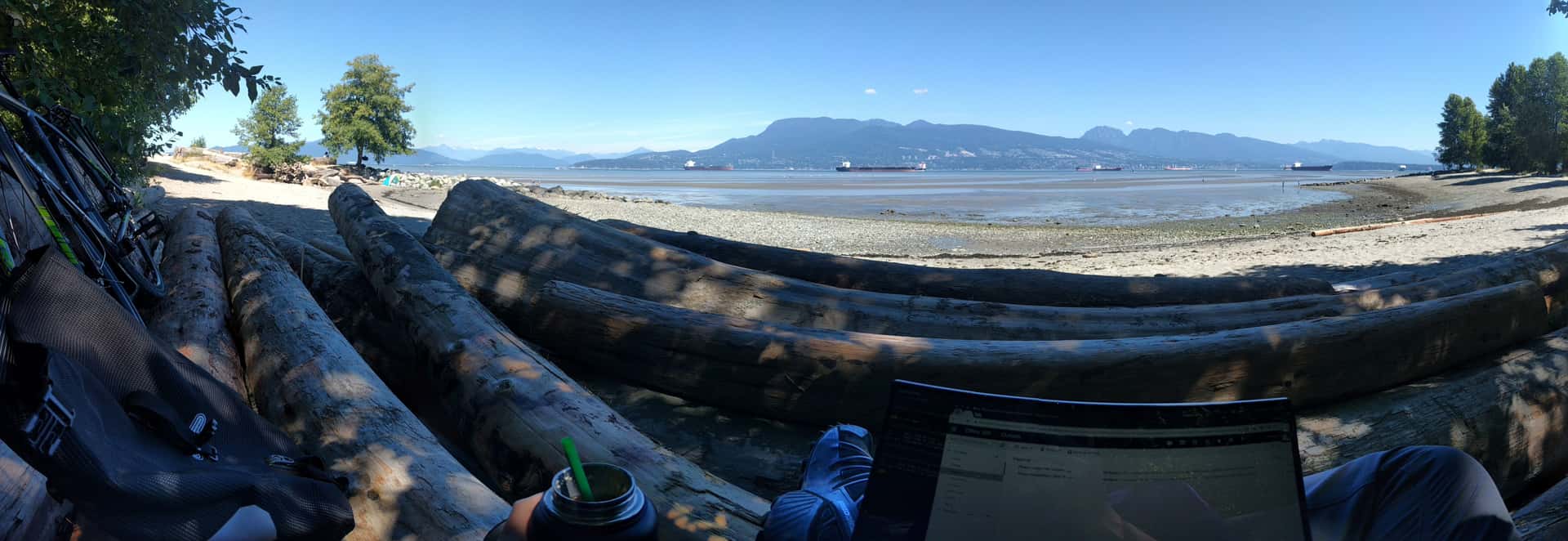 working on a laptop next to a bicycle on shaded logs at Point Grey Beach