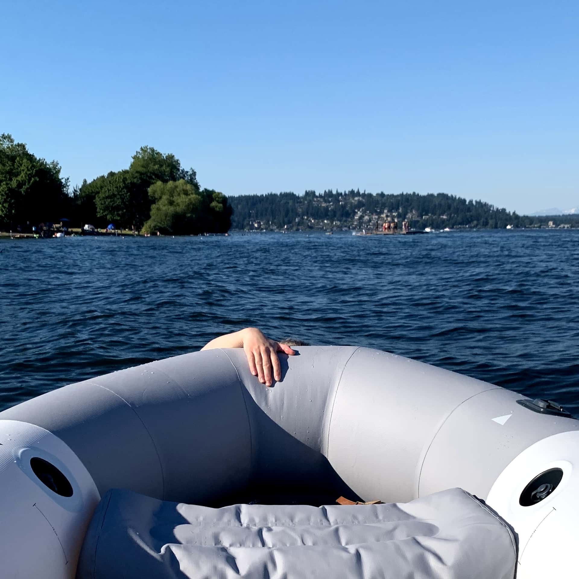 swimmer hanging by one hand from the bow of an inflatable boat on Lake Washington