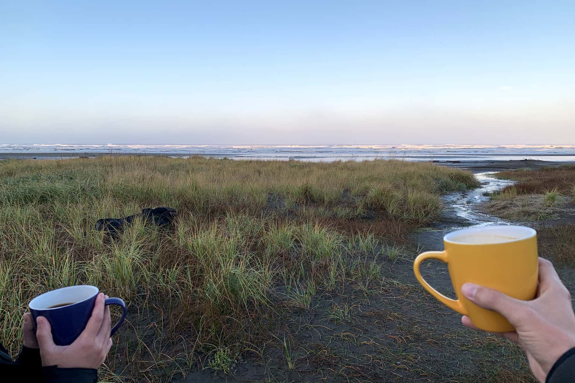 hands holding coffee in ceramic mugs on the beach at Moclips as morning sunshine begins to illuminate ocean waves