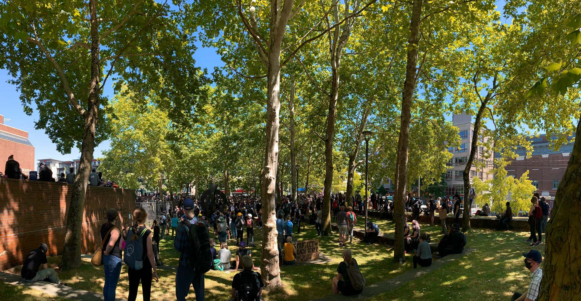 Black Lives Matter protesters await the beginning of a march under the shade of trees on the Seattle Central College campus