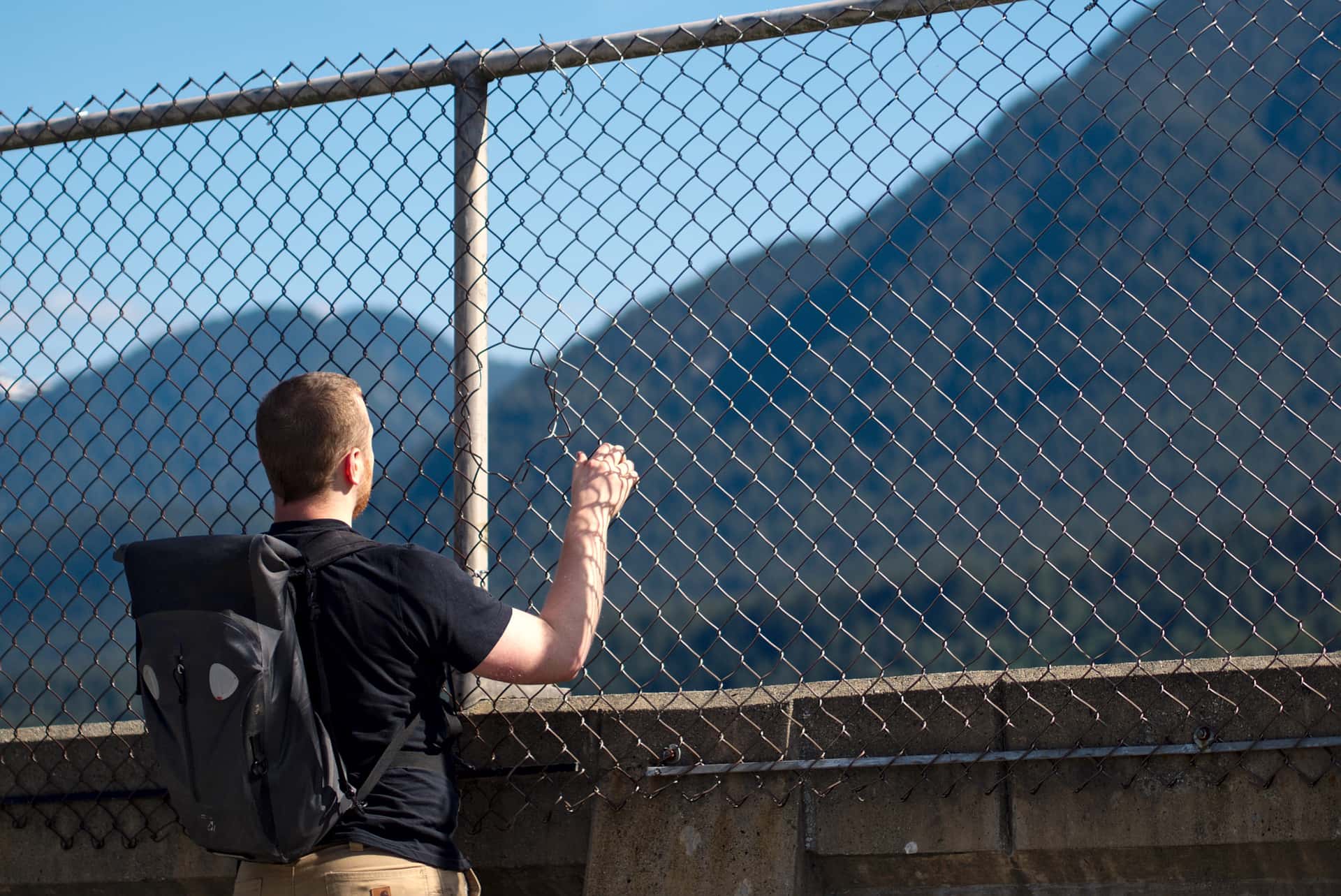 peering at Grouse Mountain through a hole in a fence on Cleveland Dam