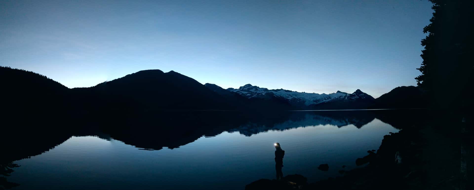 shining a headlamp from the shore of Garibaldi Lake at dawn